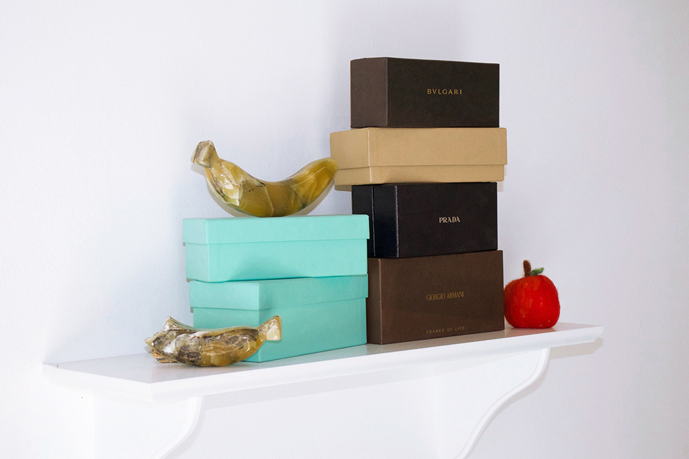 A sheflt with various designer eyeglass cases and fruit sculptures